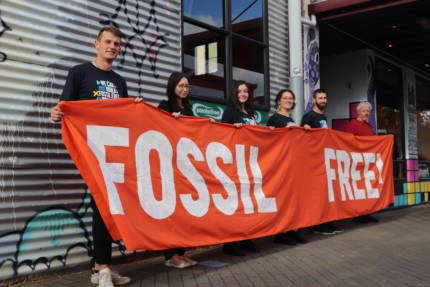 350 Te Papaioea group with 6 members holding up a large orange banner with large white painted letters reading "FOSSIL FREE!"