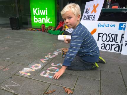 Young boy chalks 'No more fossil fuels' on the pavement outside Kiwibank in Christchurch