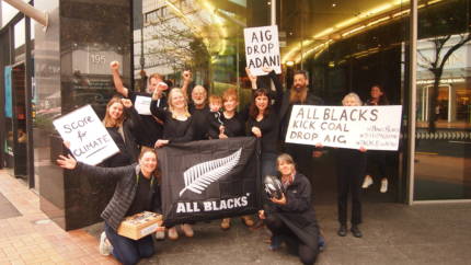 A photo of people in All Blacks gear outside NZ Rugby with a petition calling for the All Blacks to drop AIG