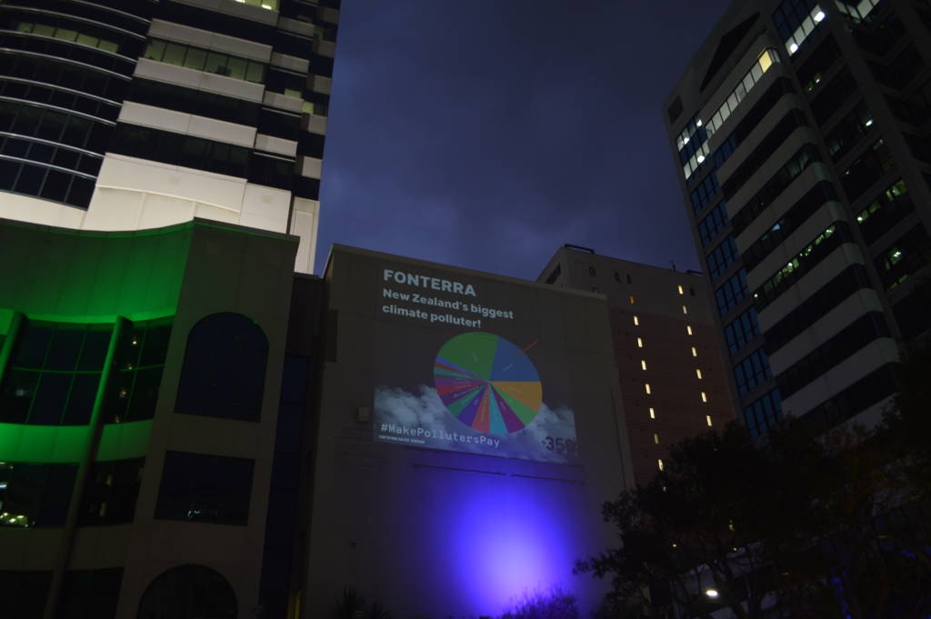 night time projection that reads Fonterra New Zealands biggest climate polluters and has a chart shoowing that Fonterra makes up a quarter of all emissions