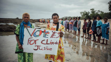 Two Vanuatuan people holding up a sign "vote yes for climate justice".