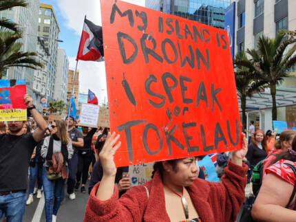 Tokelaun woman holds up red sign at a climate march - "My island is drown I speak for Tokelau"
