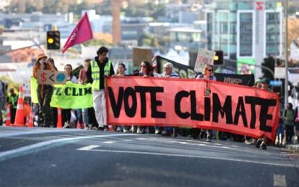 Protesters at a climate march holding up a big red banner that reads 'VOTE CLIMATE'.